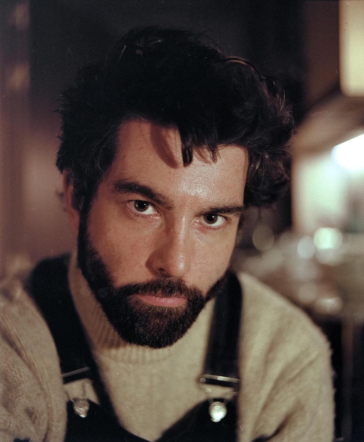 A man with a beard and dark hair looks directly at the viewer.