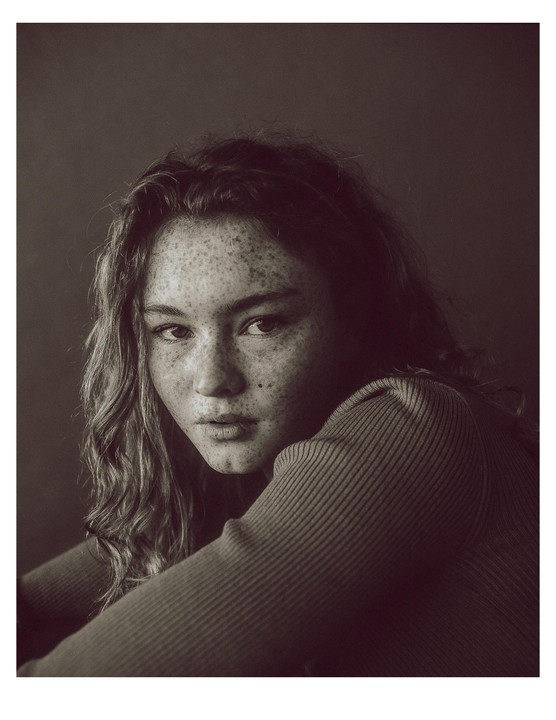 A young woman with freckles and curly hair looks directly at the viewer.