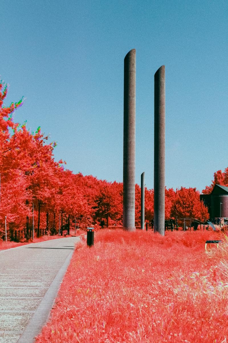 Three tall, cylindrical structures stand amidst vibrant red foliage and grass under a clear blue sky.