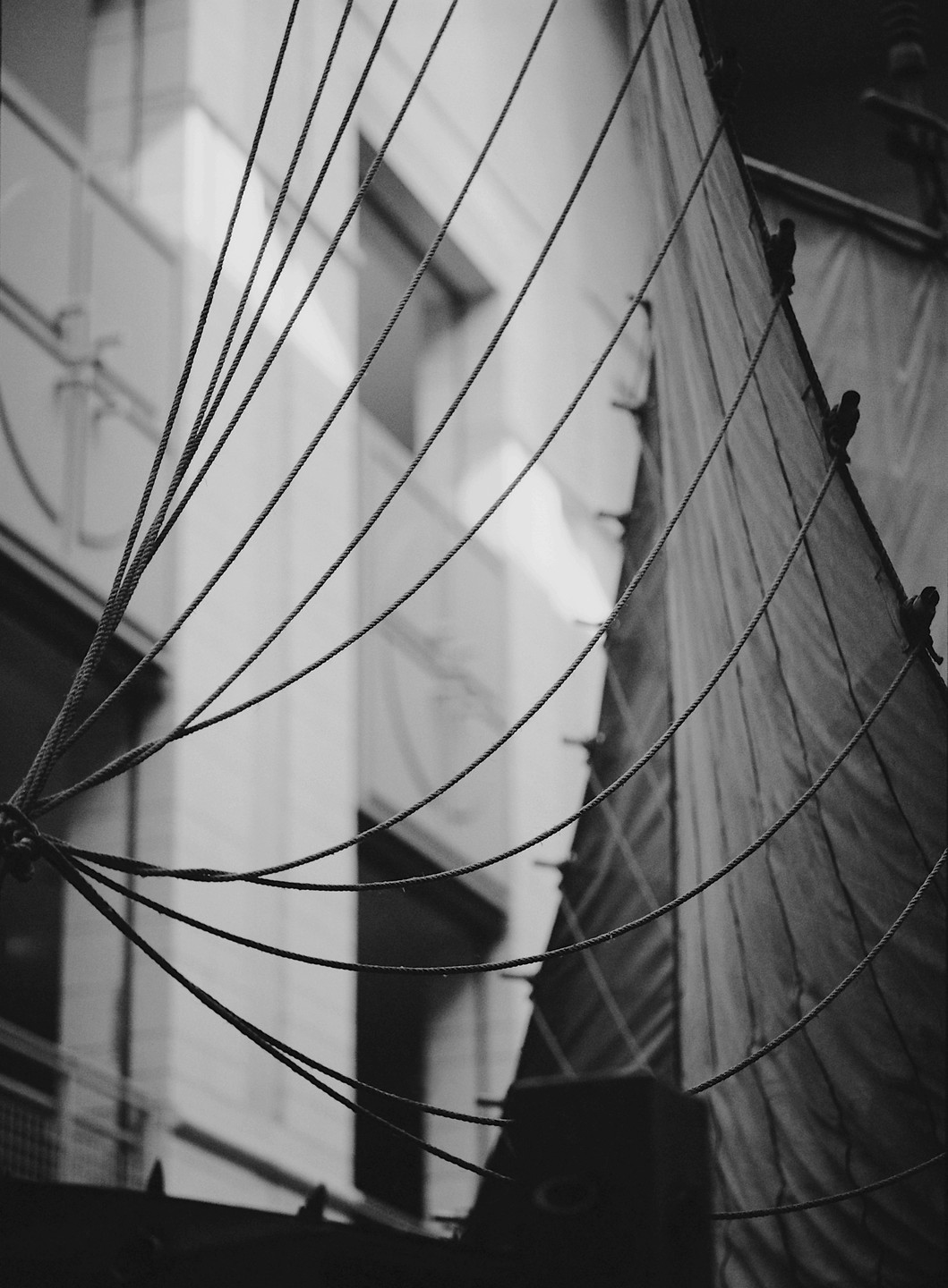 A close-up view shows ropes and a sail against a blurred building.