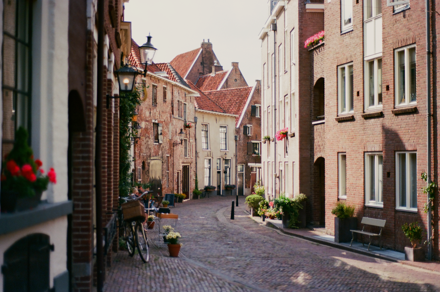 A narrow, cobbled street is lined with old brick buildings, some with red tile roofs and window boxes.
