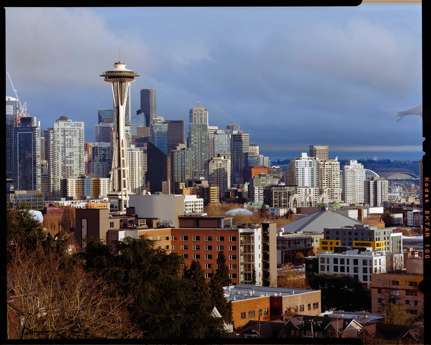 The Seattle skyline is visible with the Space Needle prominently featured among other buildings and a cloudy sky.