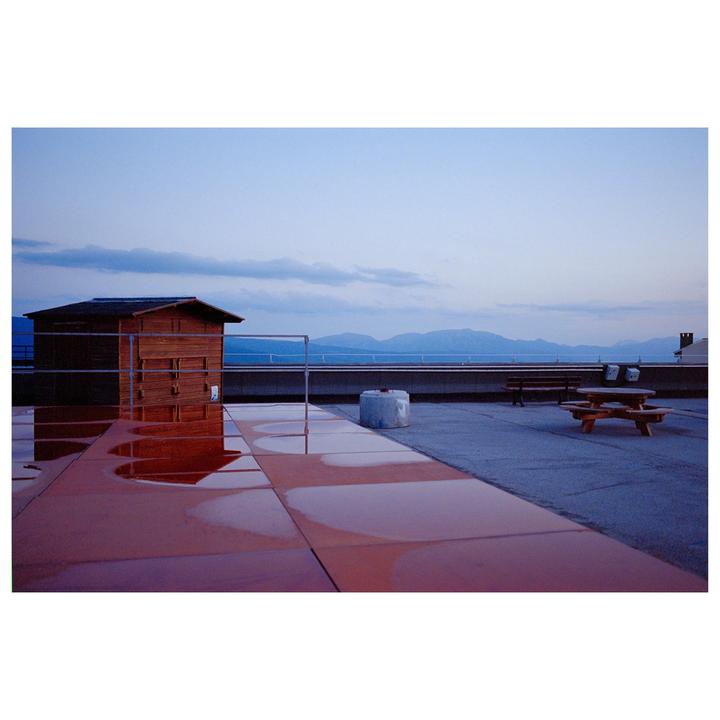A wooden shed and a picnic table sit on a rooftop with mountains in the distance under a blue sky.
