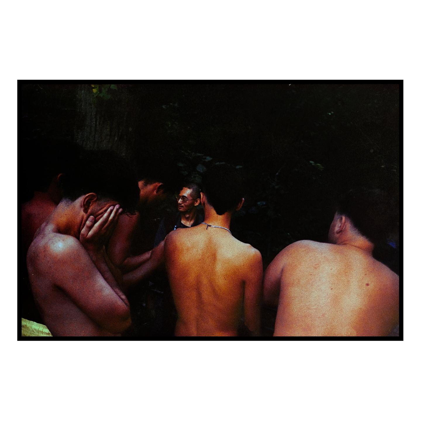 Four men are gathered outdoors, with one man covering his face with his hands.