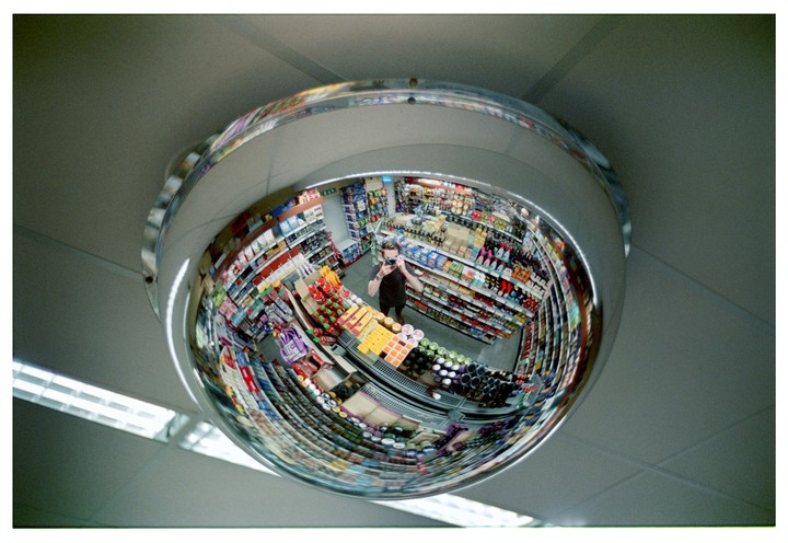 A man takes a self-portrait in a convex security mirror in a store.