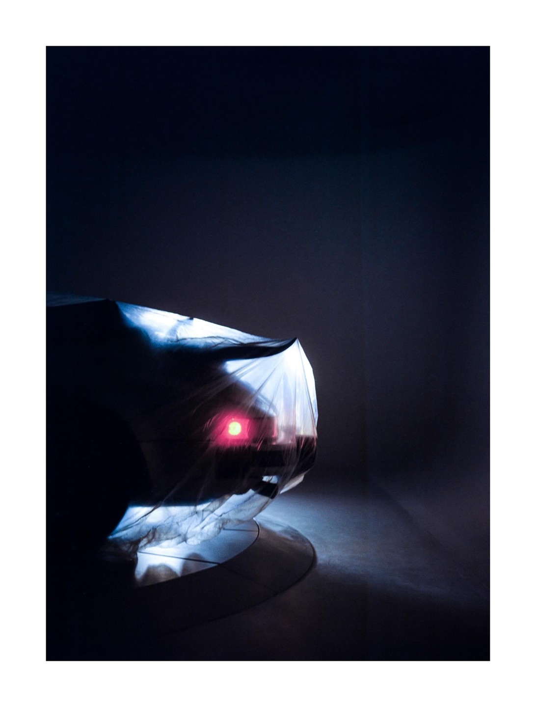 A car covered with a white sheet is illuminated by a red light from within.