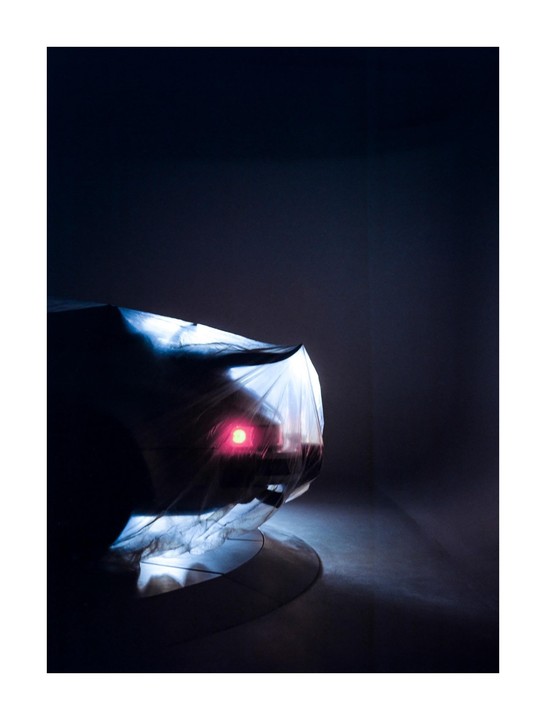 A car covered with a white sheet is illuminated by a red light from within.