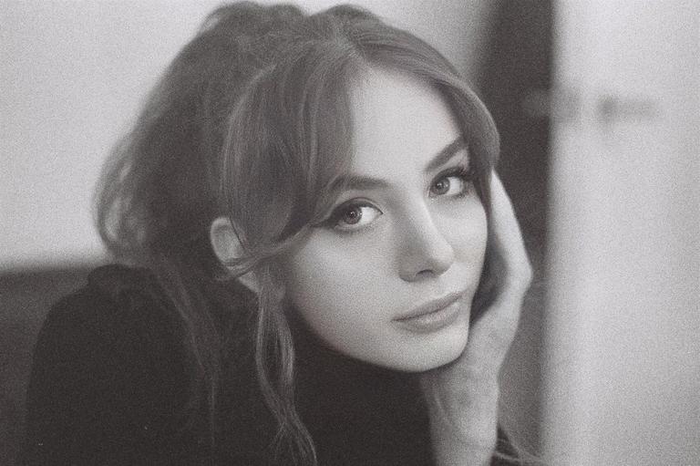 A woman with bangs and long hair looks at the viewer, resting her head on her hand.
