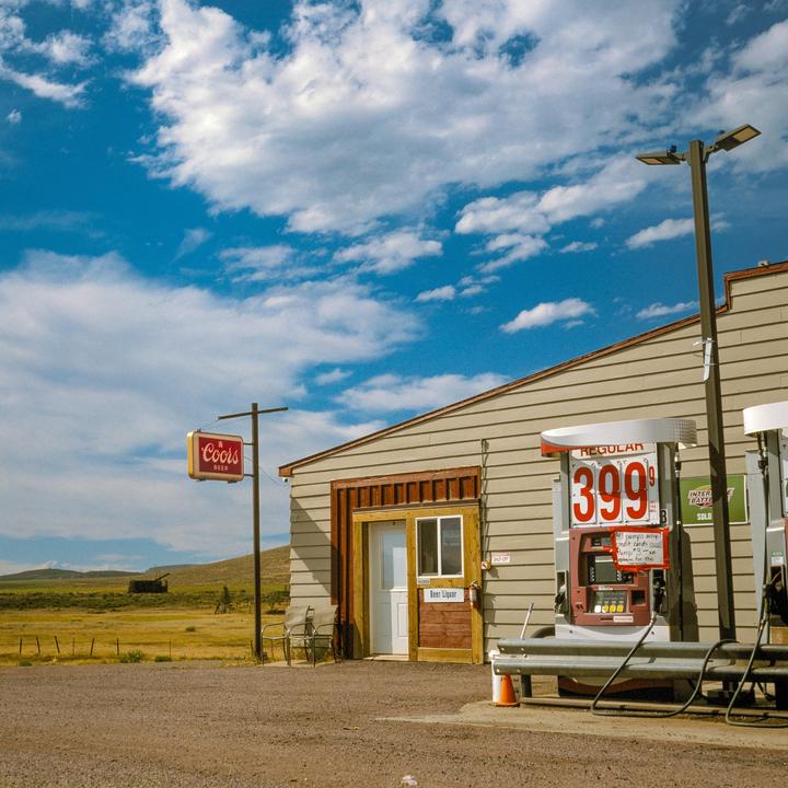 A gas station and store with a Coors beer sign stands next to a field under a blue sky with clouds.