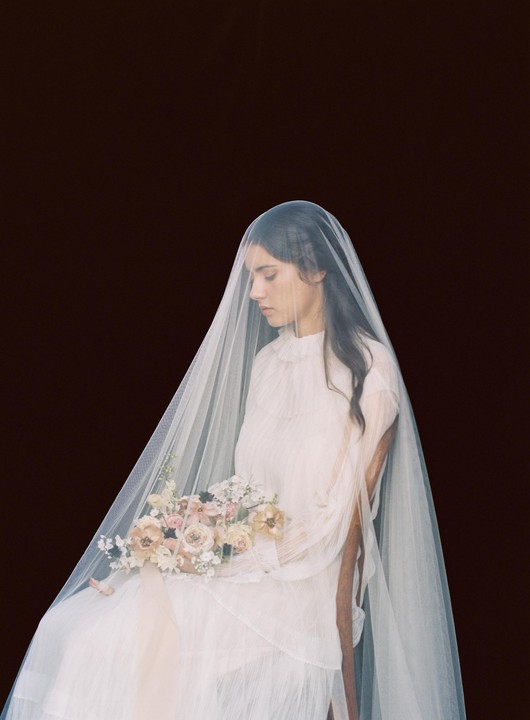 A woman in a white dress and veil holds a bouquet of flowers.