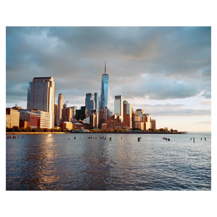 The Lower Manhattan skyline is visible across the water under a cloudy sky.