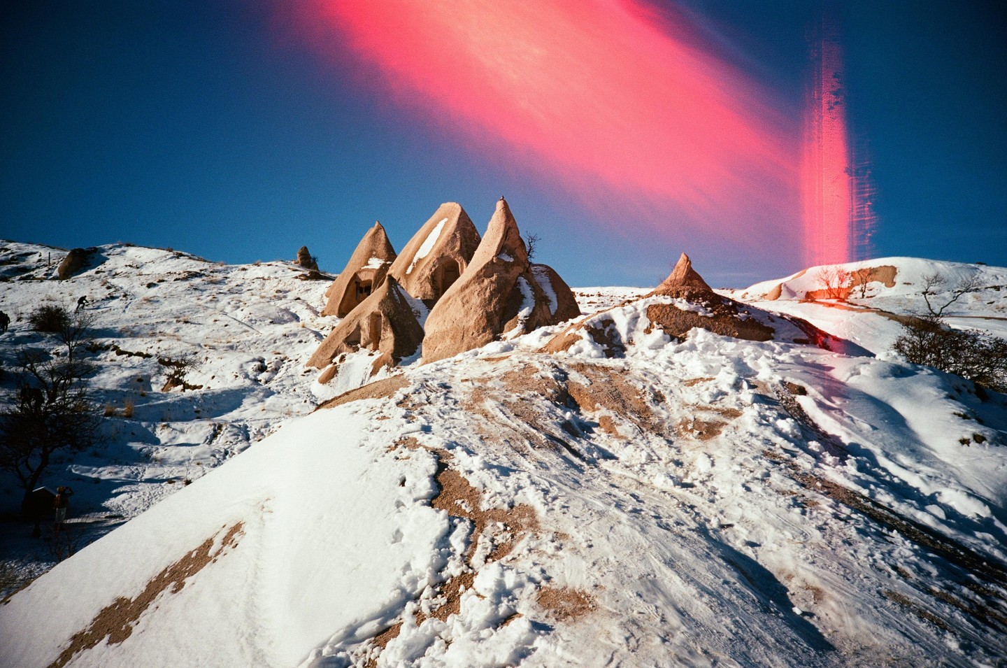 A snowy landscape features several conical rock formations under a bright blue sky with a red light leak.