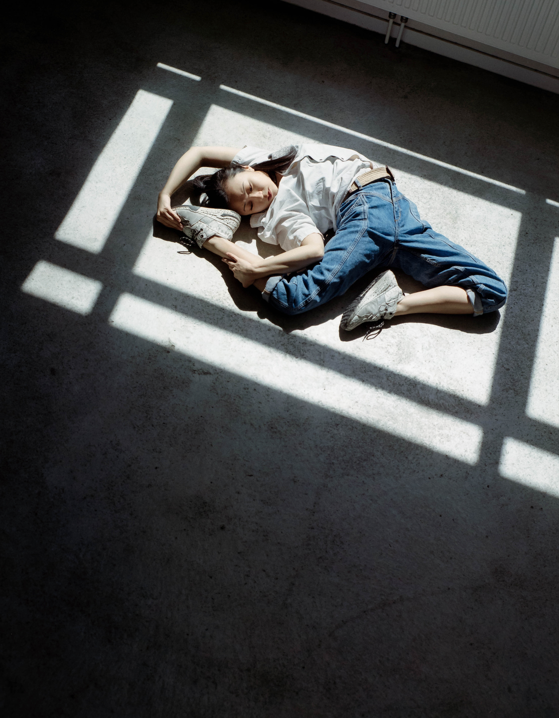 A woman lies on a concrete floor with strong shadows cast over her body.