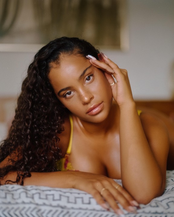 A woman with curly hair and freckles lies on a patterned surface, resting her head on her hand.