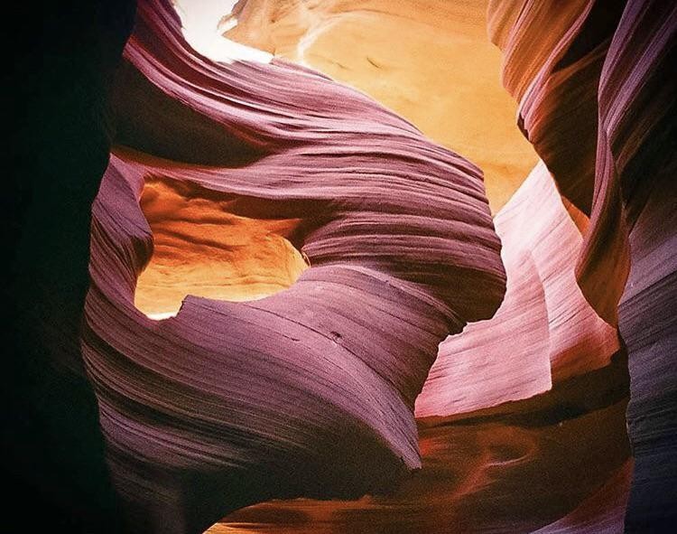 A narrow slot canyon with swirling rock formations is illuminated by light from above.