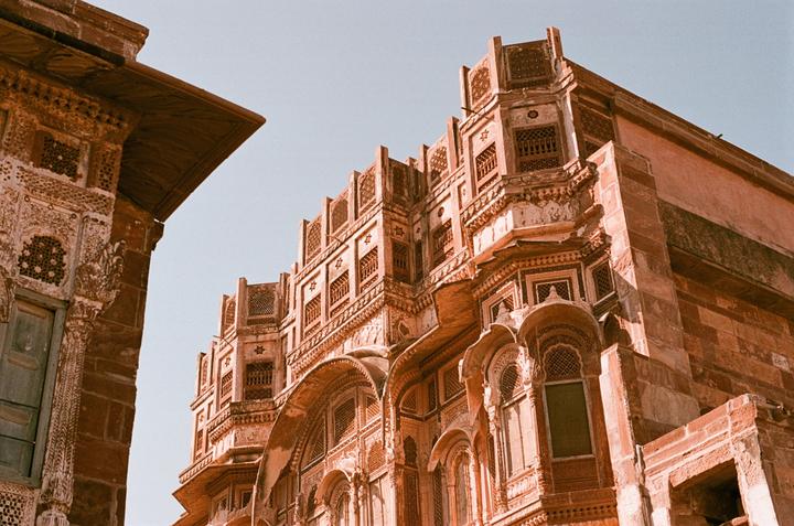 Two ornate buildings with intricate carvings and windows are visible against a clear sky.