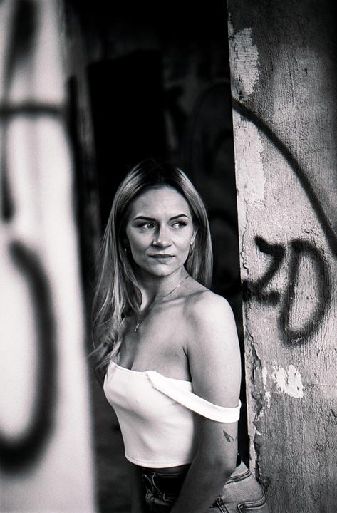 A woman in a white top stands in an abandoned house with graffiti on the wall.