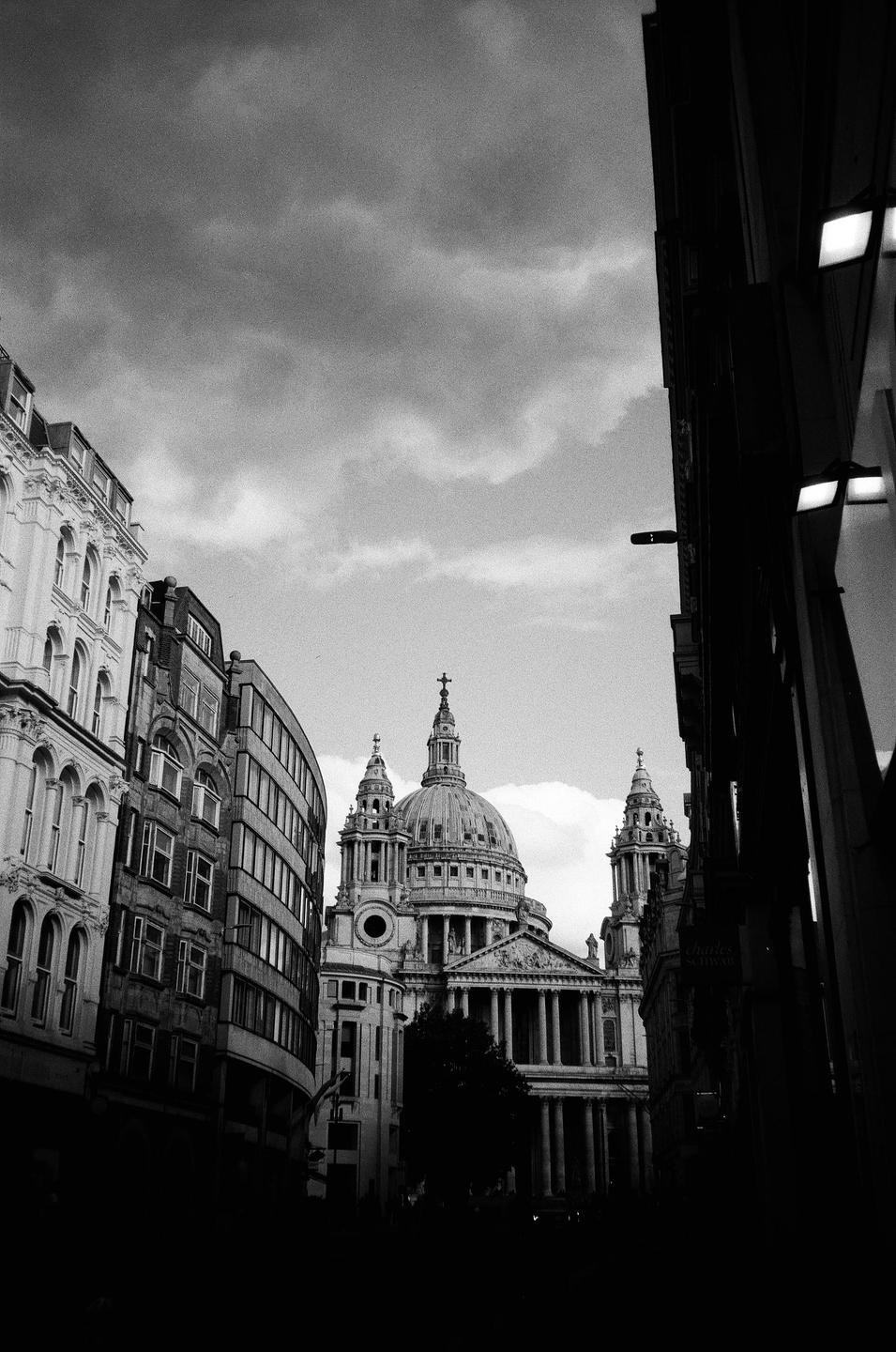 St Paul's Cathedral is visible between two tall buildings under a cloudy sky.