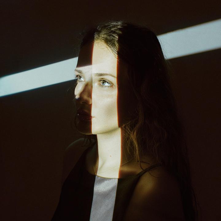 A woman's face is illuminated by a projector creating stripes of light and shadow.