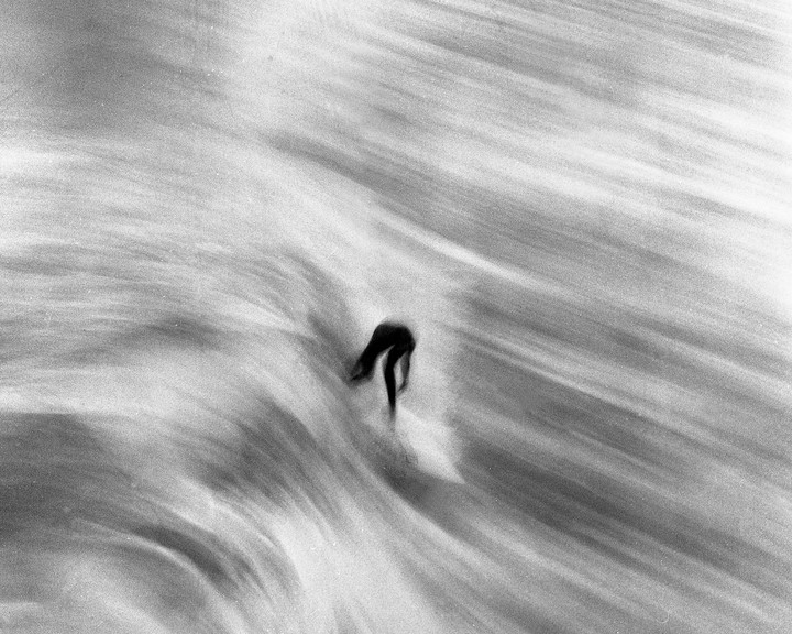 A surfer rides a wave in a black and white photograph with motion blur.