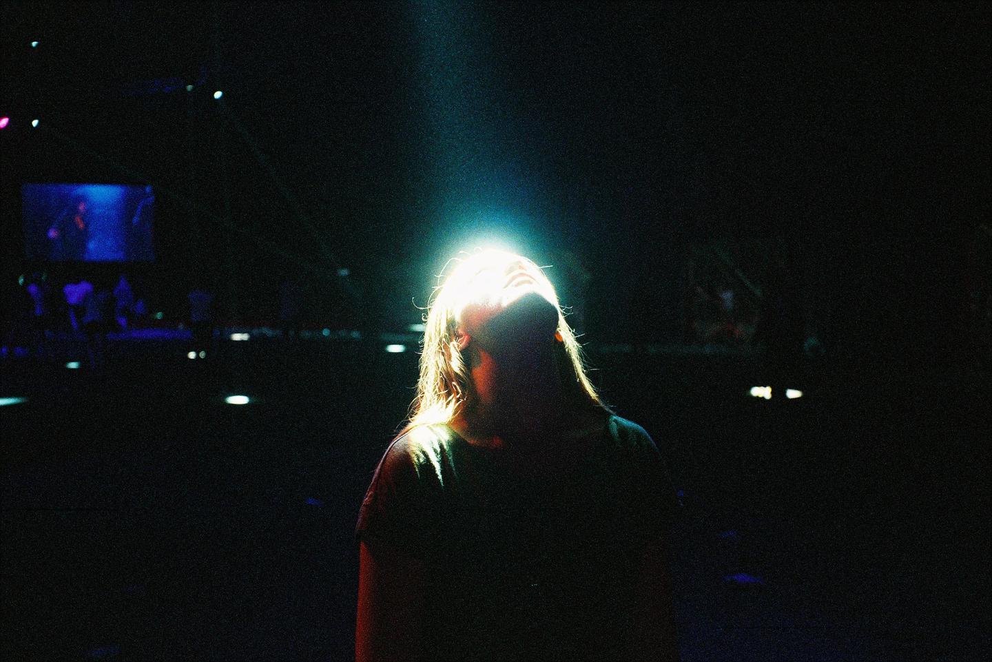 A woman with long hair is illuminated by a bright light from above, with her head tilted back.