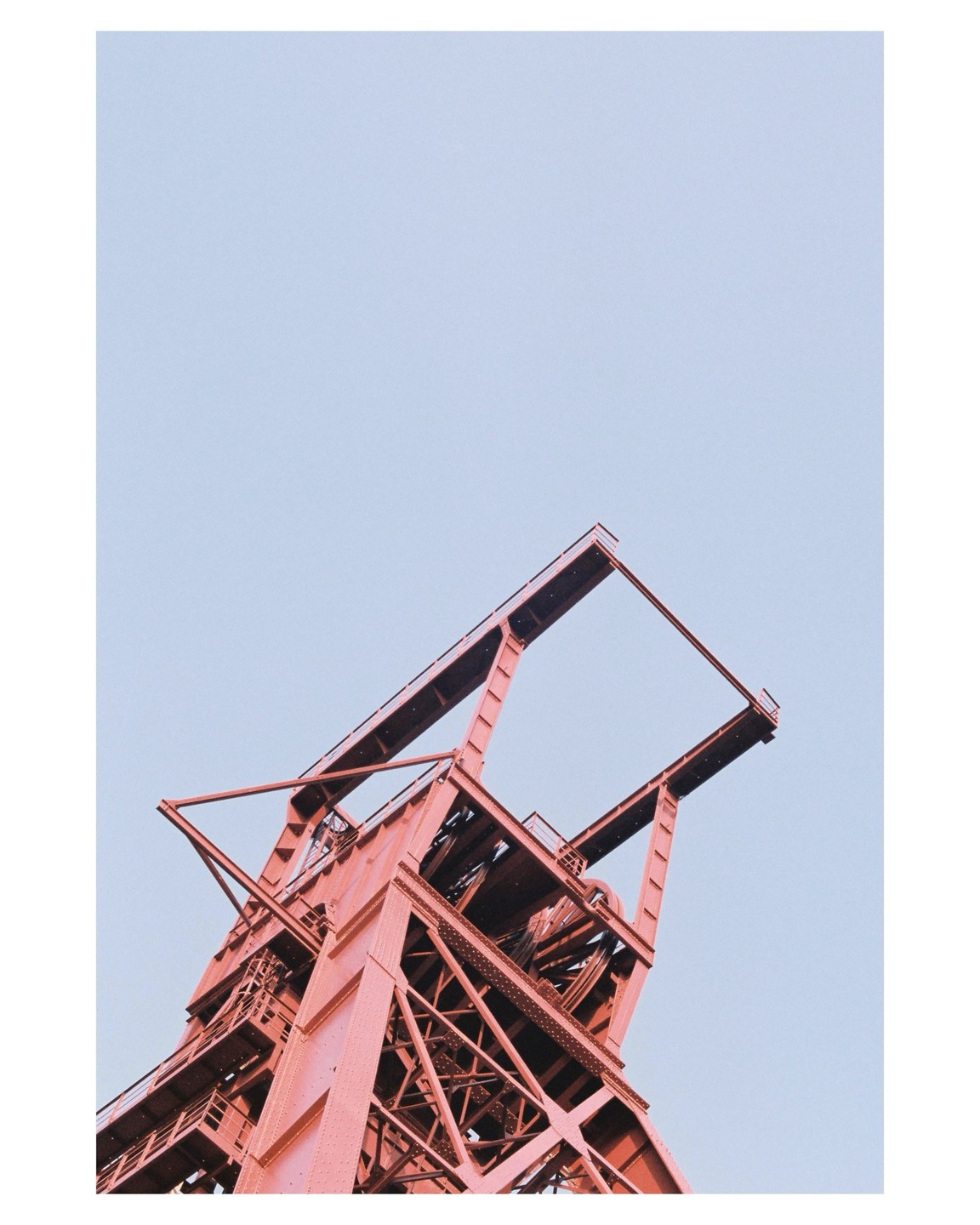 A red industrial structure is viewed from below against a pale blue sky.