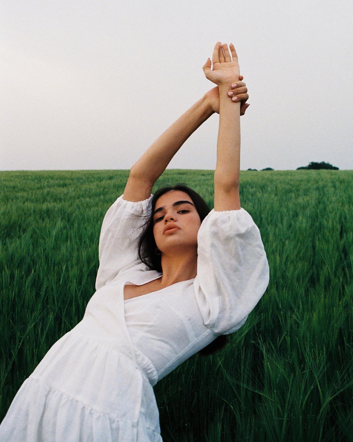 A woman in a white dress poses with her arms raised in a field of green crops.