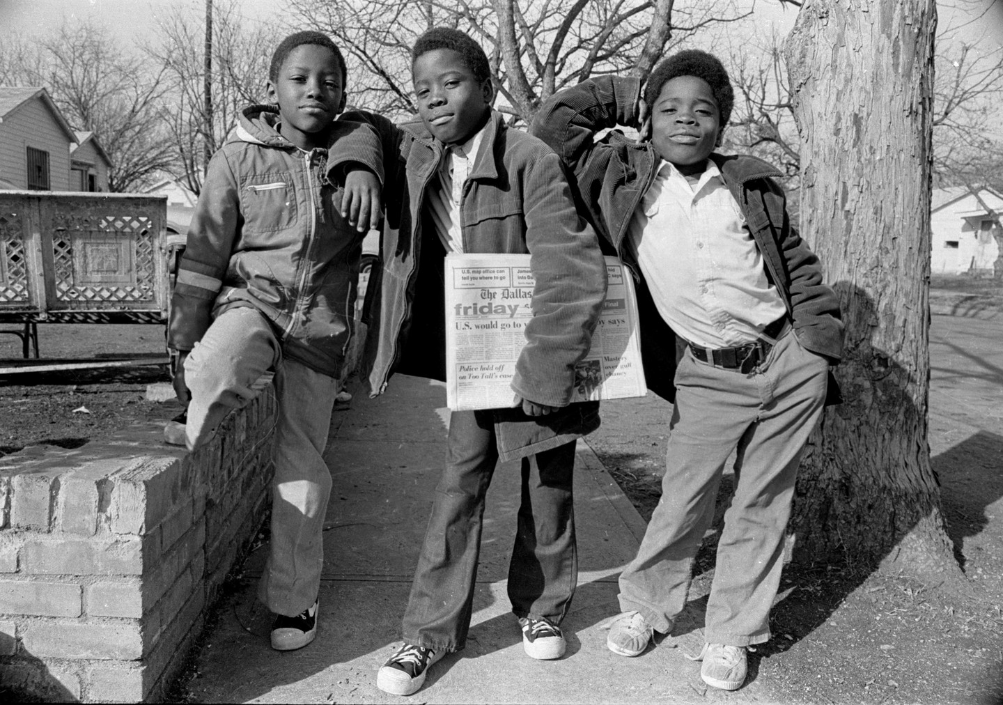 Three boys pose for a portrait on a street in Dallas, one holding a newspaper.
