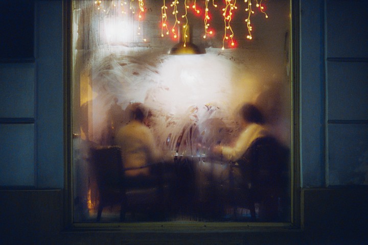Two people are sitting at a table behind a steamy window adorned with string lights.