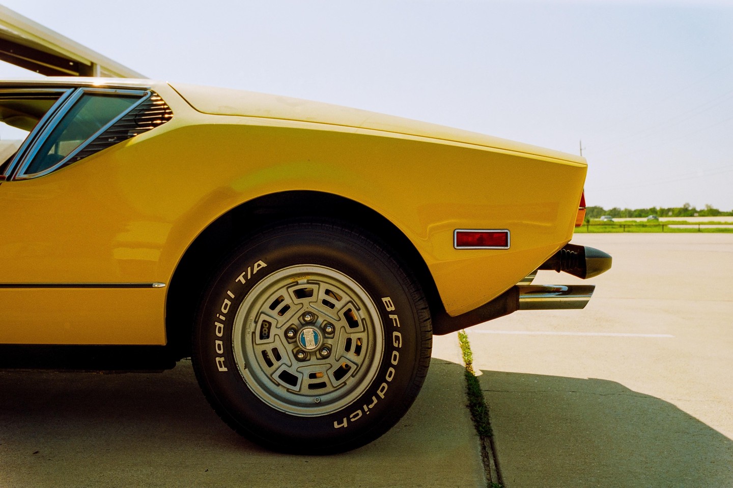 The rear quarter panel of a yellow sports car is parked on an asphalt surface under a clear sky.