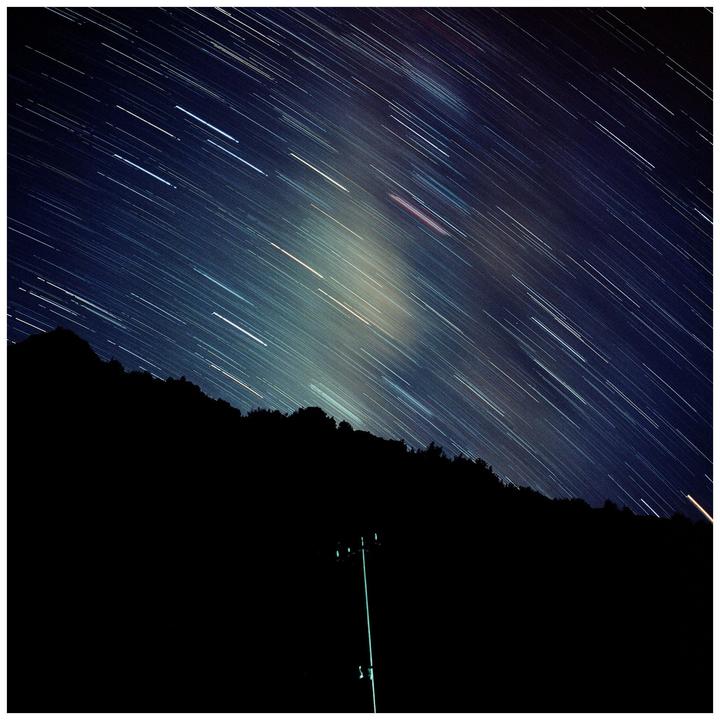 A long exposure photograph captures star trails across a night sky above a dark mountain silhouette and a utility pole.