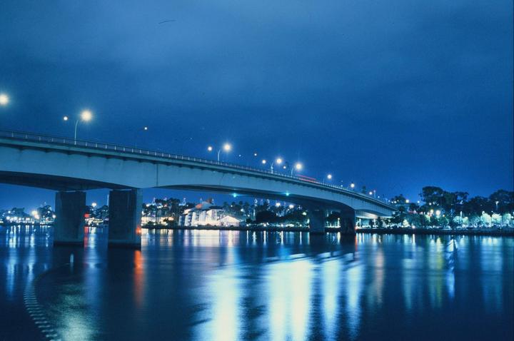 A bridge with streetlights crosses over water at night, with city lights visible on the distant shore.