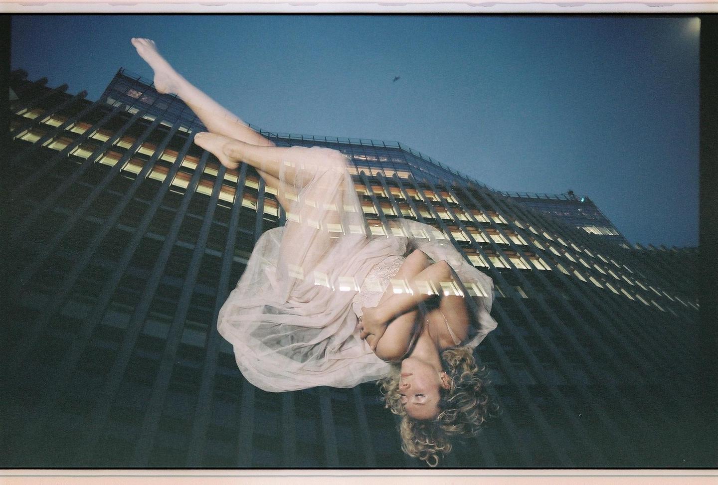A woman in a light-colored dress is superimposed over a building with many windows.