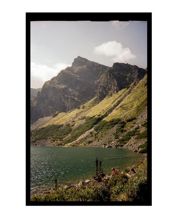 A mountain lake is surrounded by steep, rocky slopes with patches of green vegetation under a bright sky.
