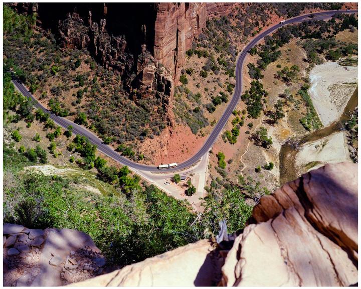 A winding road with two buses on it is visible from a high vantage point overlooking a canyon.