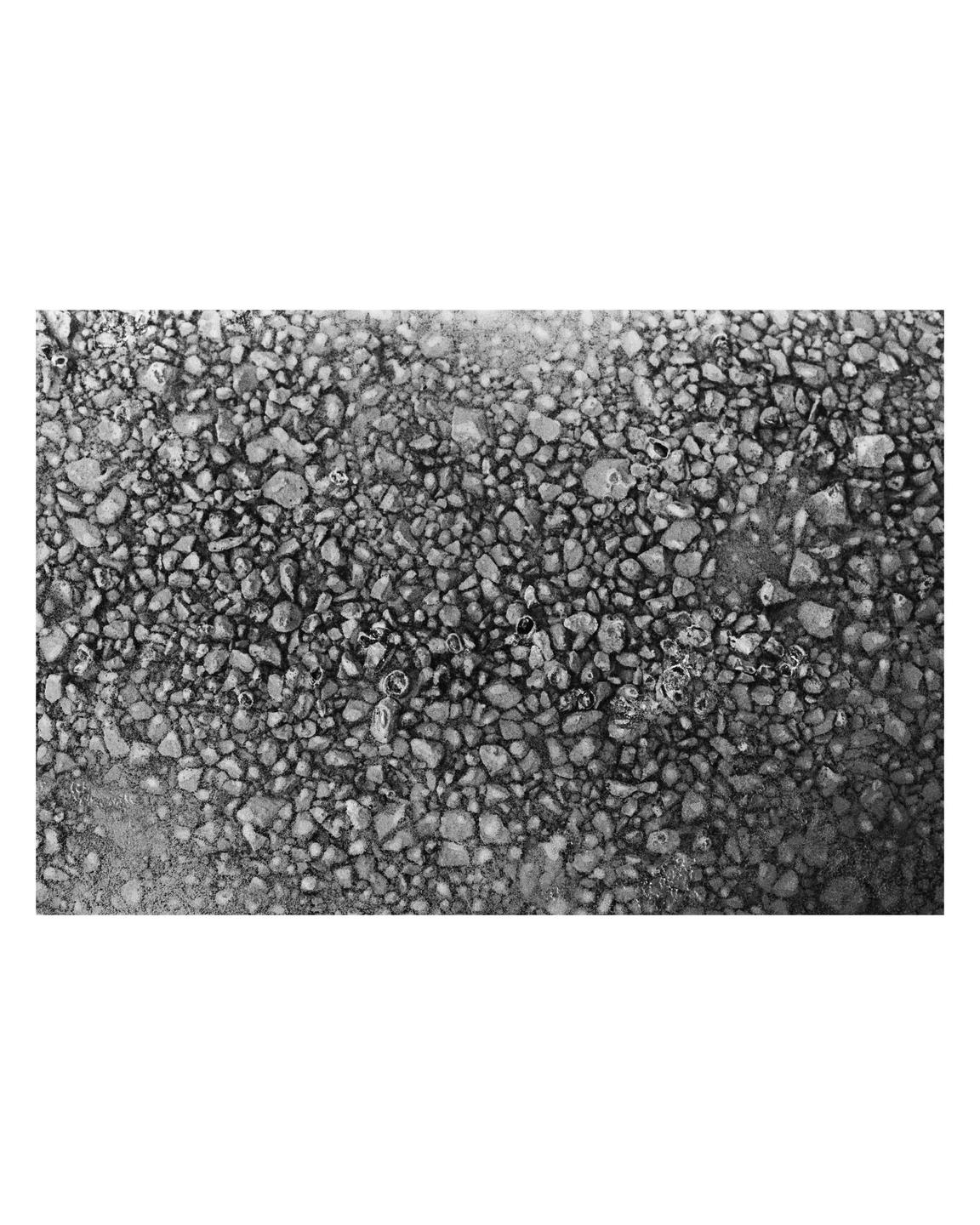 A close-up, high-angle view shows a textured surface of small, irregular stones with some water and bubbles.