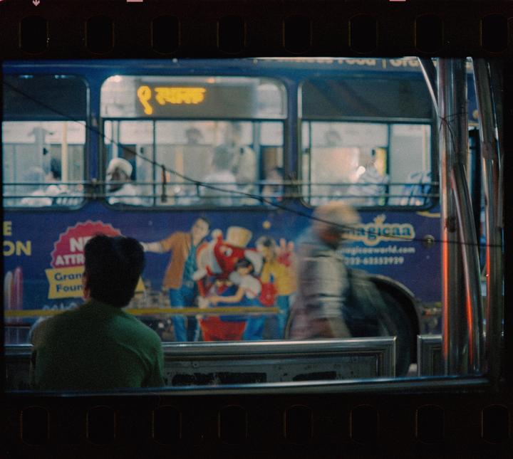 A person sits on a bus looking out at another bus with passengers and an advertisement.