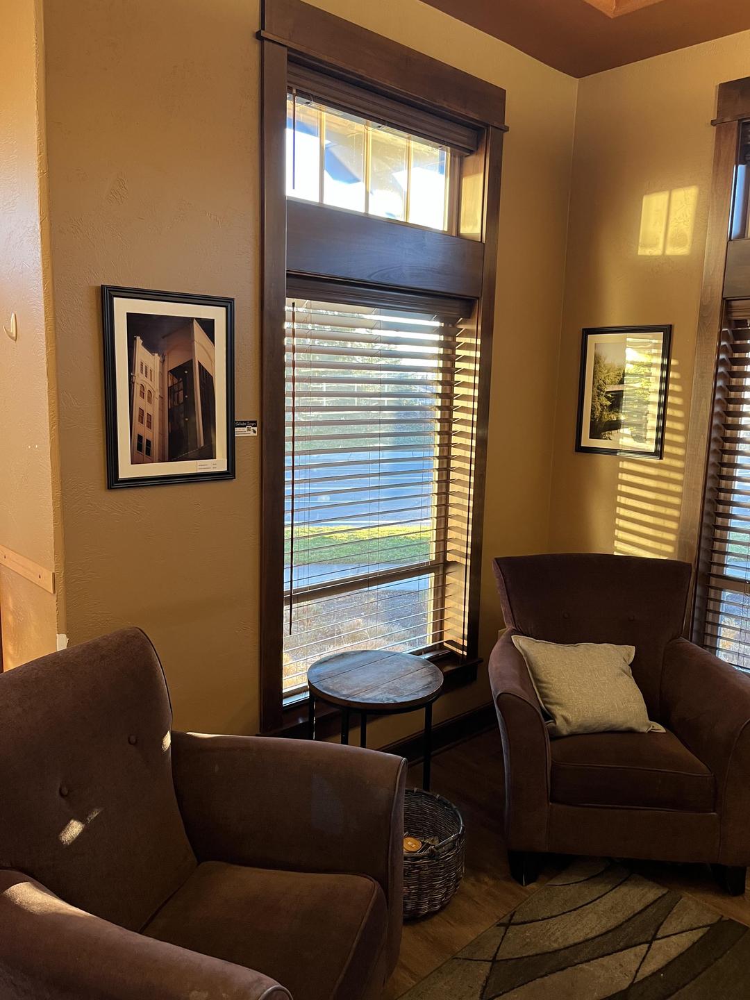 Sunlight streams through a window with blinds, illuminating two armchairs and a small table in a cozy room.