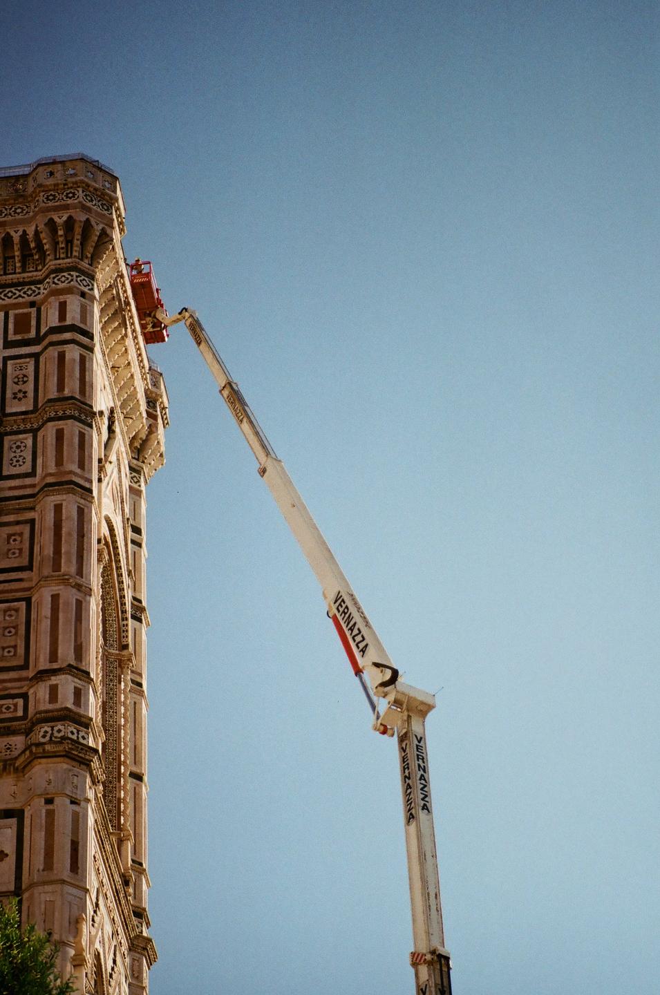 A construction crane extends towards the top of a building with intricate architectural details under a clear sky.