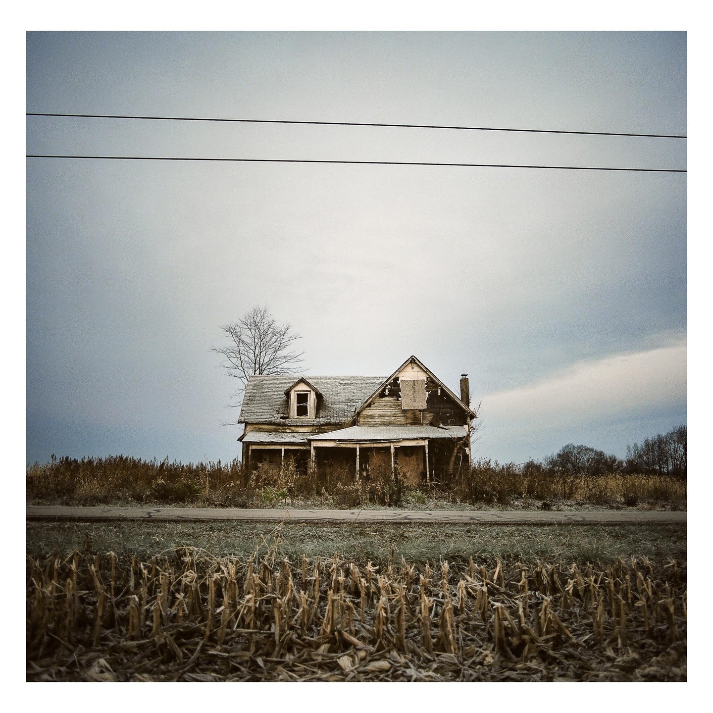 An abandoned house stands in a field under a cloudy sky.