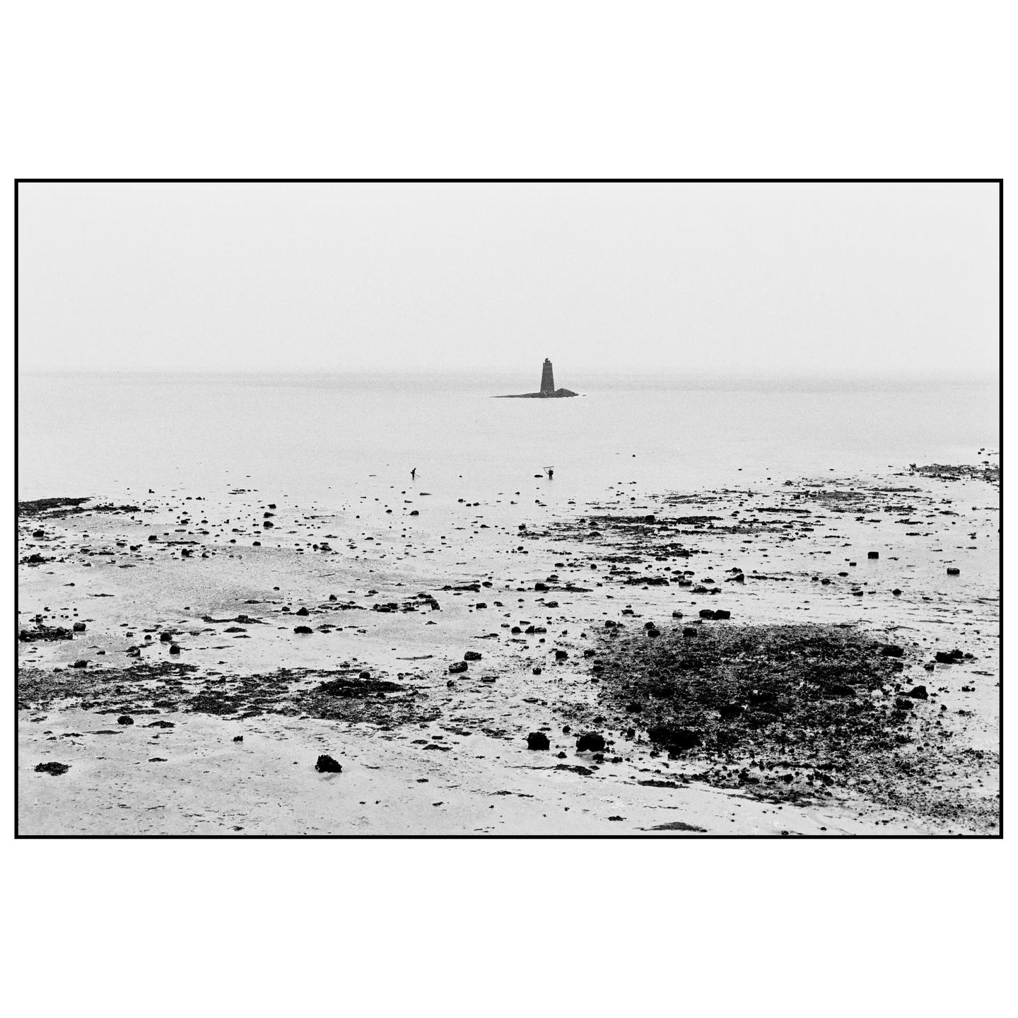 A black and white landscape shows a rocky beach with a lighthouse in the distance and two people walking on the shore.