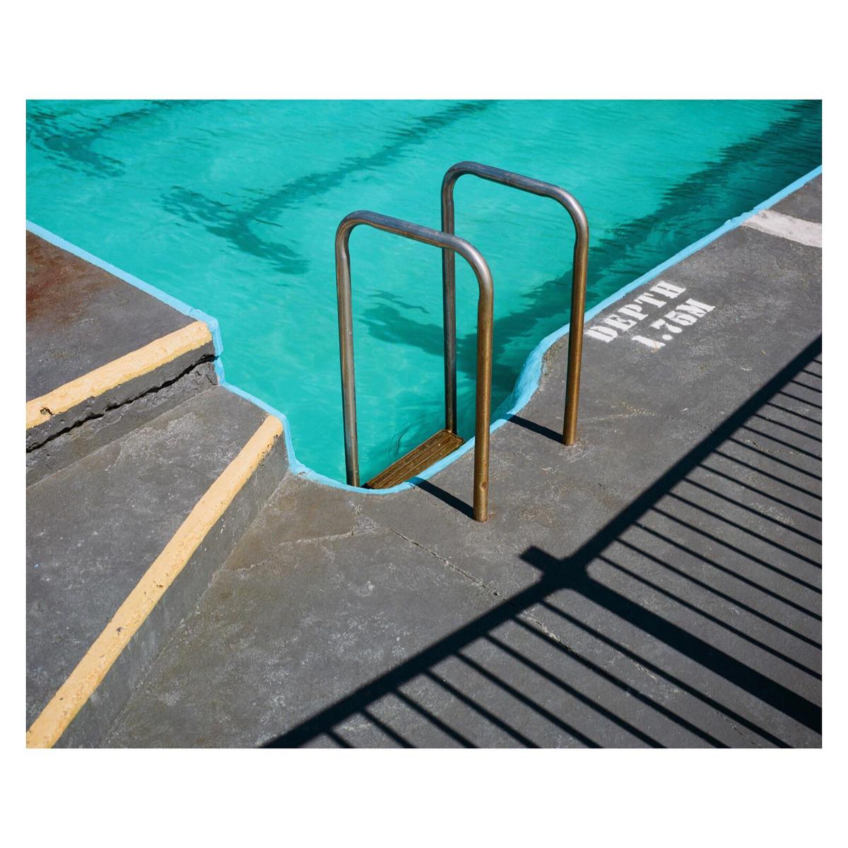 A swimming pool with turquoise water has a metal ladder and the word "DEPTH" painted on the concrete edge.