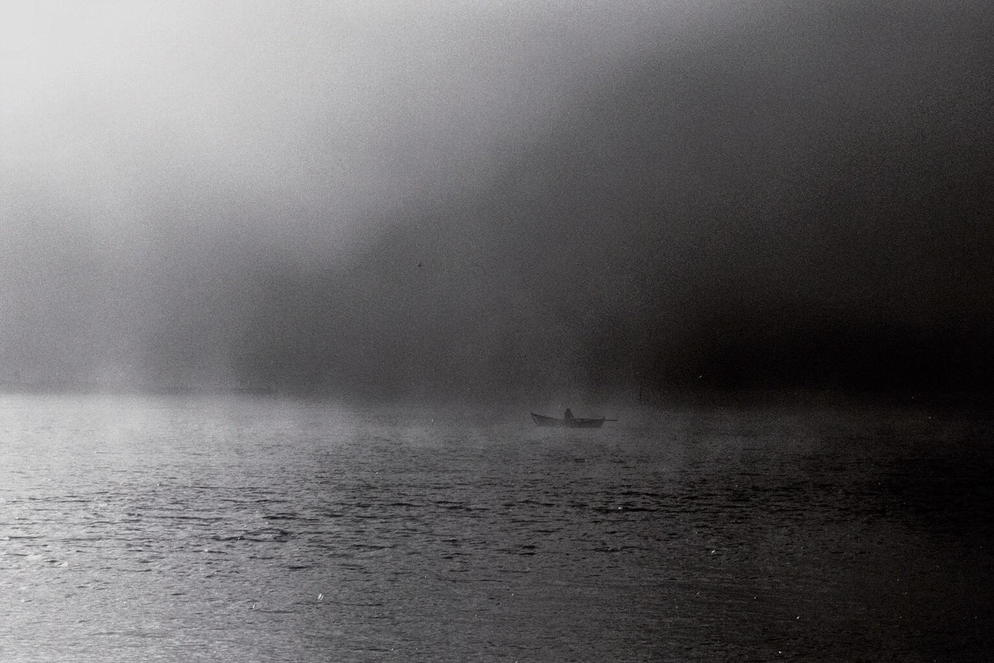 A lone person in a small boat navigates through a vast, foggy body of water.