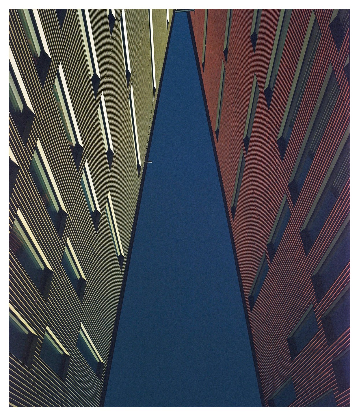 Two tall buildings with many windows create a narrow triangular gap against a dark blue sky.