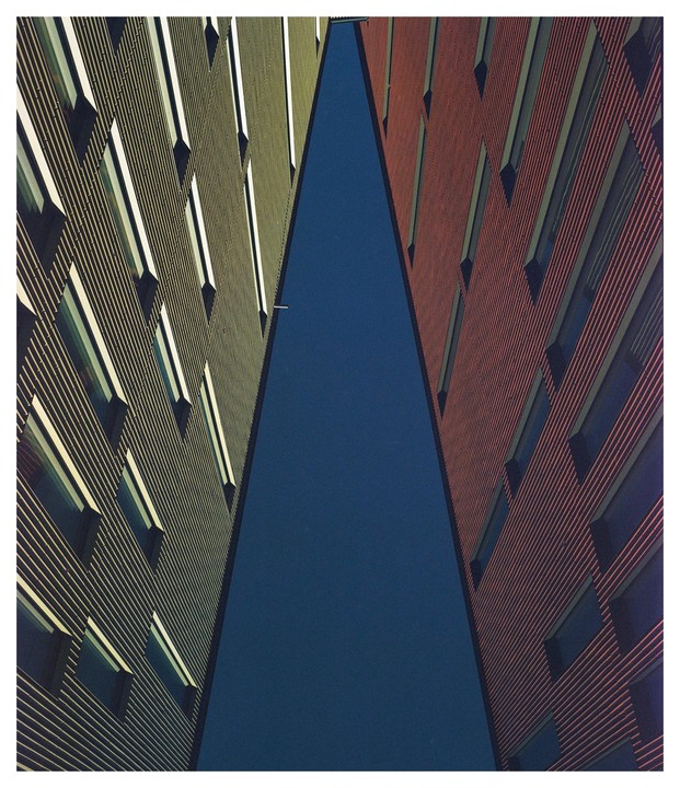 Two tall buildings with many windows create a narrow triangular gap against a dark blue sky.