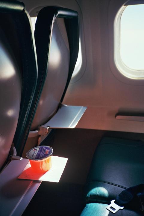 A small cup of orange juice sits on a tray table next to an airplane seat.