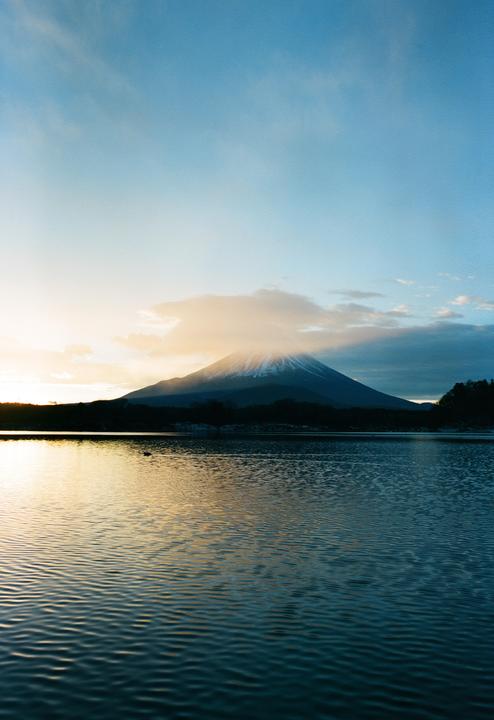 Mount Fuji rises above a lake with a golden hour sky.