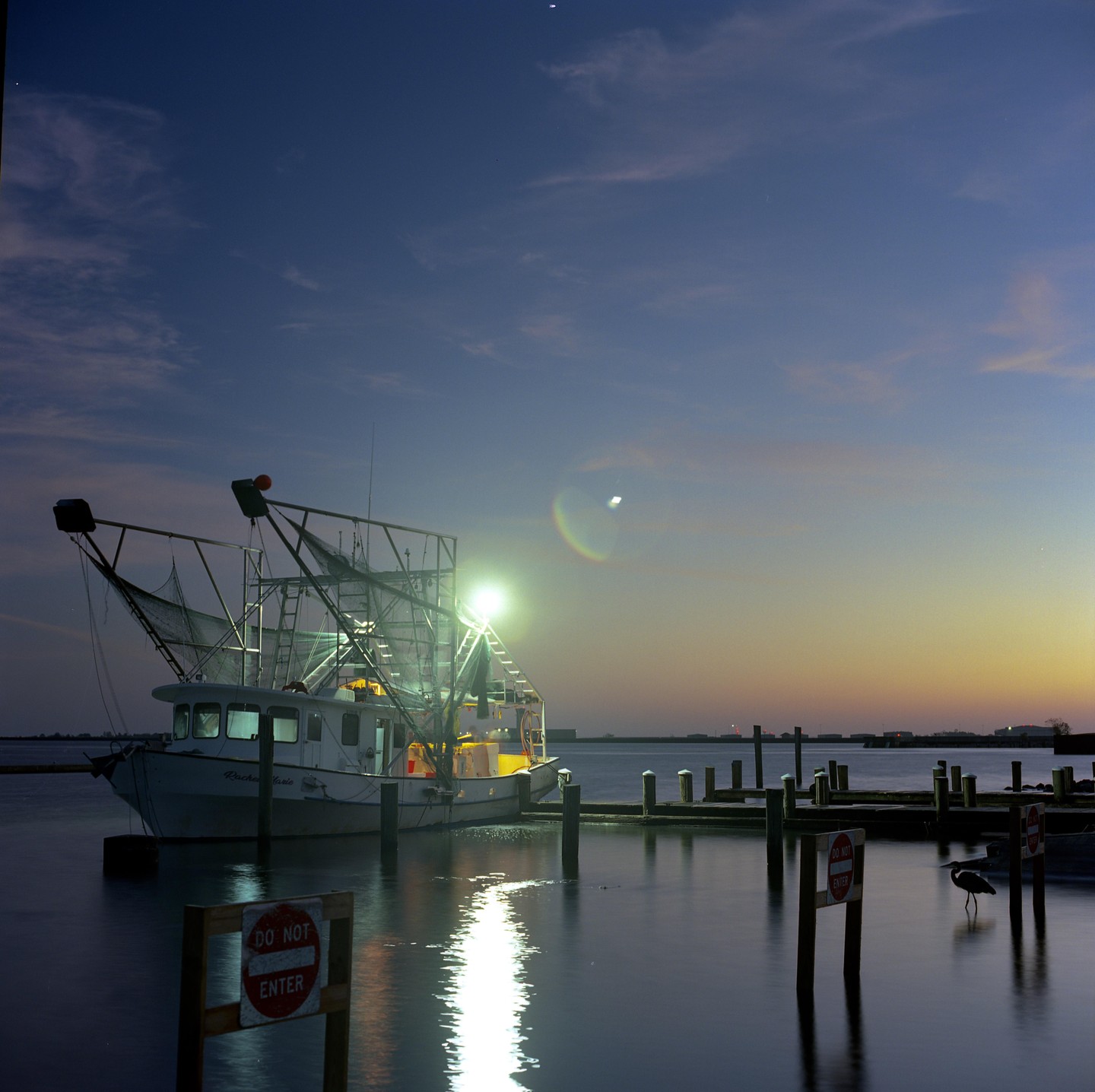 A fishing boat is docked at a pier with a heron standing in the water at dawn.