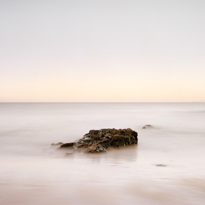A large rock sits in the ocean with a smooth, misty water effect.