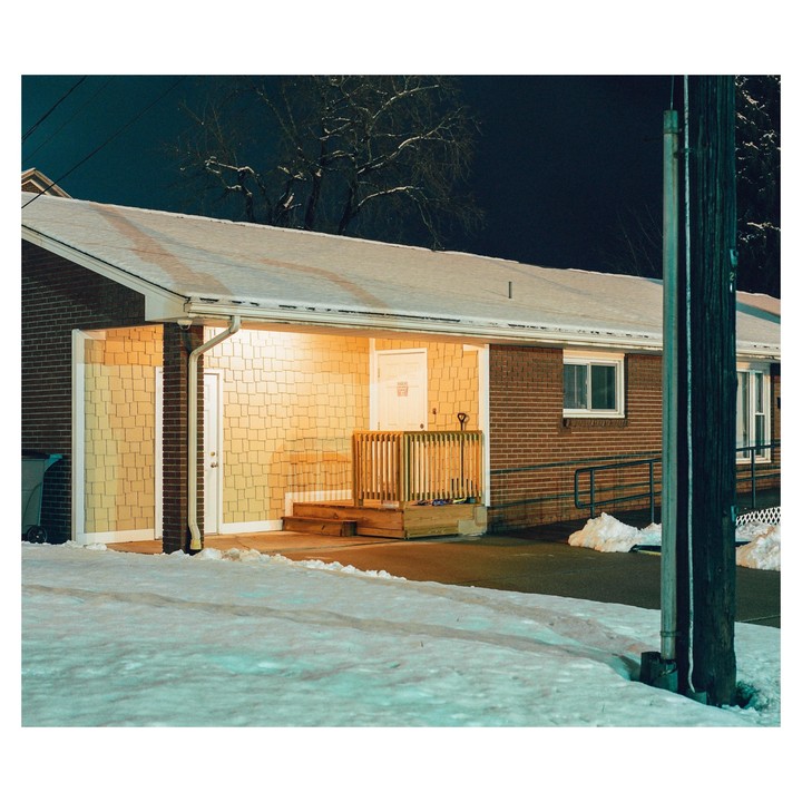 A brick building with a snow-covered roof and porch is illuminated at night.